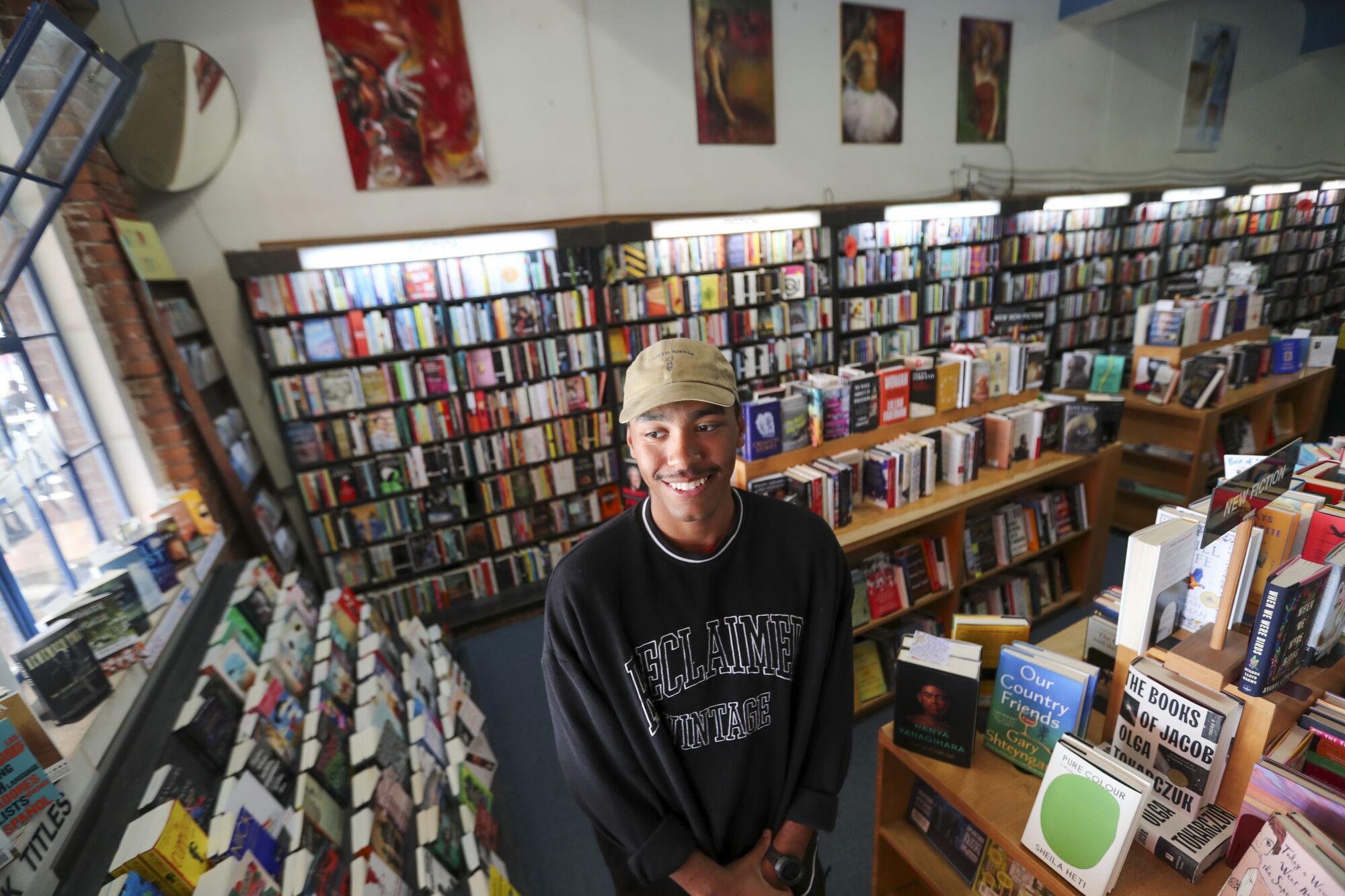 A man wearing a beige hat and black sweatshirt in a bookstore.