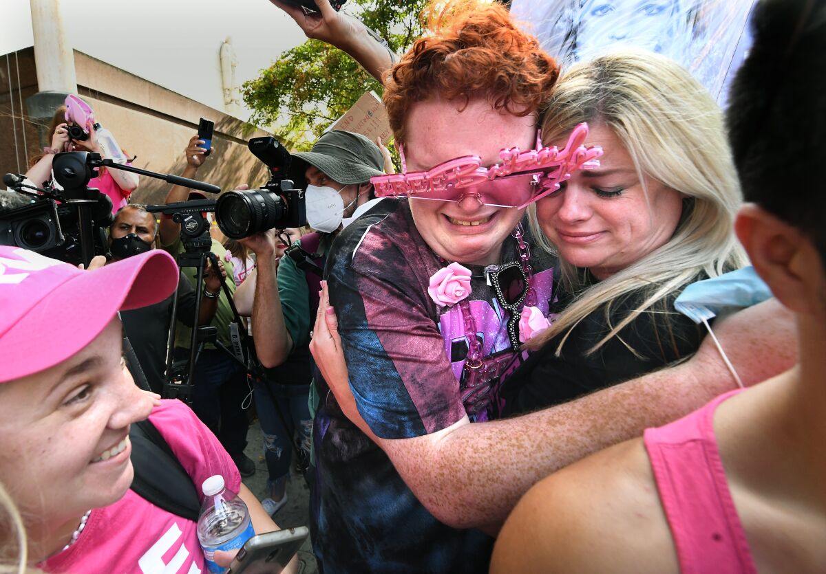 A person wearing Britney Spears sunglasses cries as they hug a woman.