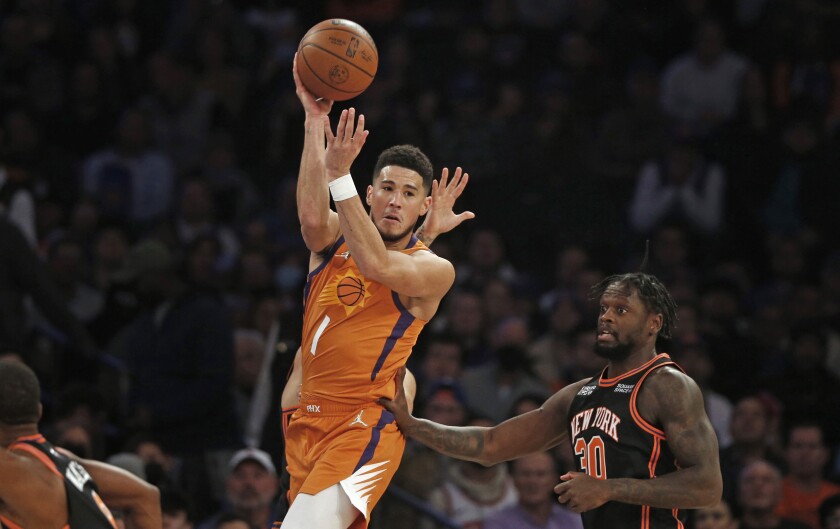 Devin Booker (1), de los Suns de Phoenix, pasa al balón frente a Julius Randle (30), de los Knicks de Nueva York, durante la primera mitad del juego de la NBA, el viernes 26 de noviembre de 2021, en Nueva York. (AP Foto/John Munson)