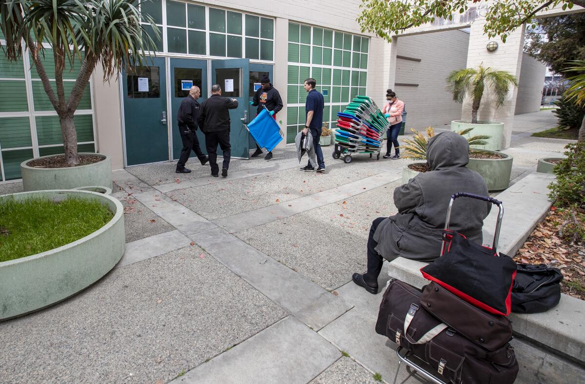 A homeless woman waits as city workers and volunteers with the Salvation Army set up cots at Westwood Recreation Center, which is now doubling as a shelter because of the coronavirus. 