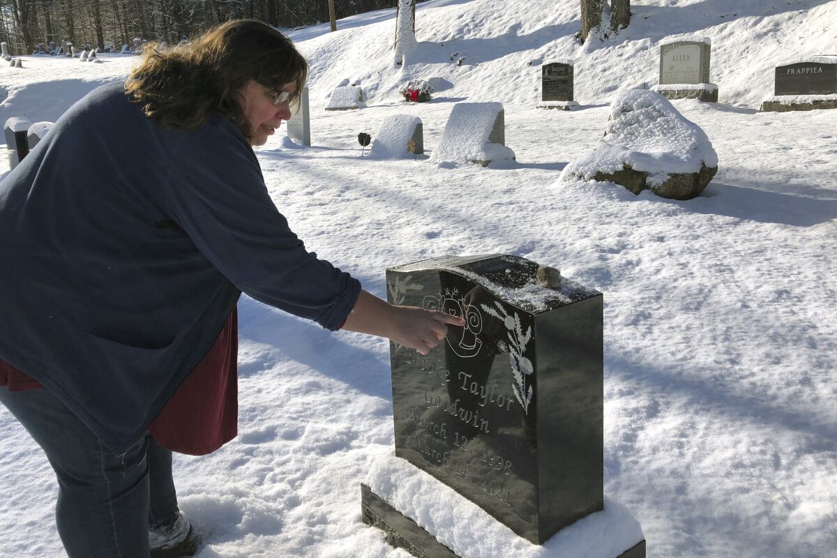 A woman pointing to the design on a black headstone in a snow-covered cemetery.