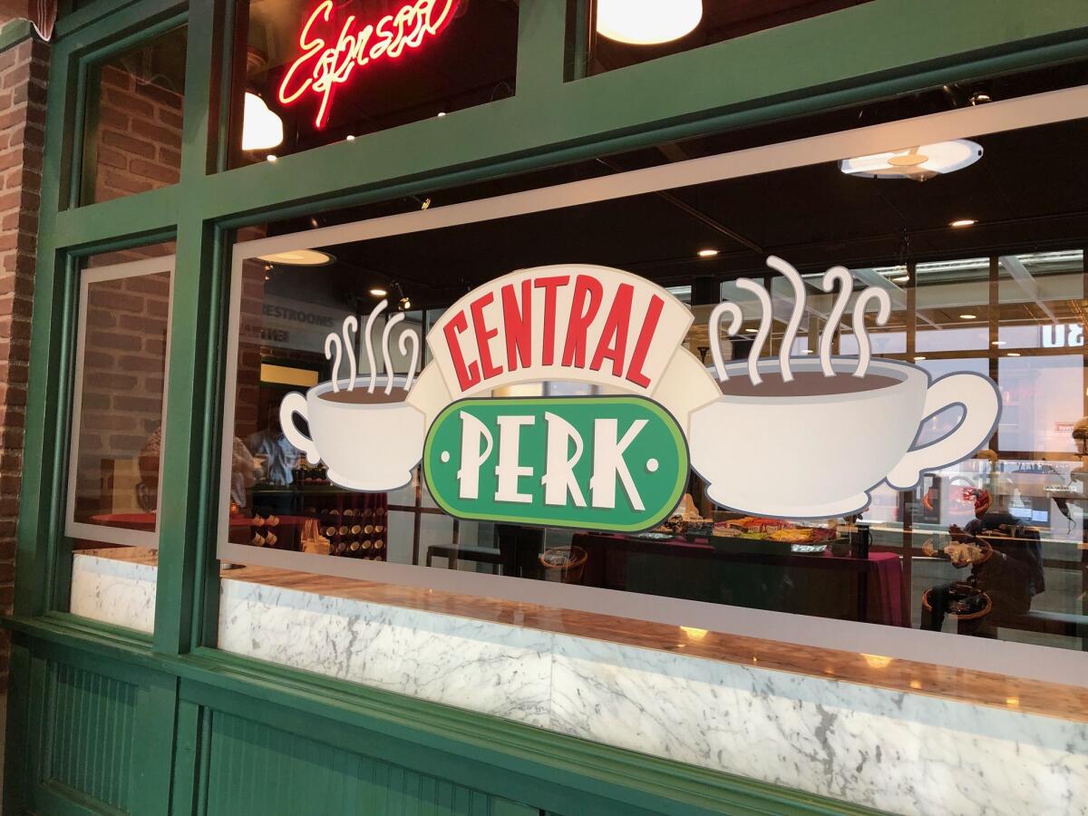 The words Central Perk are painted on a large storefront window and flanked by two steaming coffee cup images