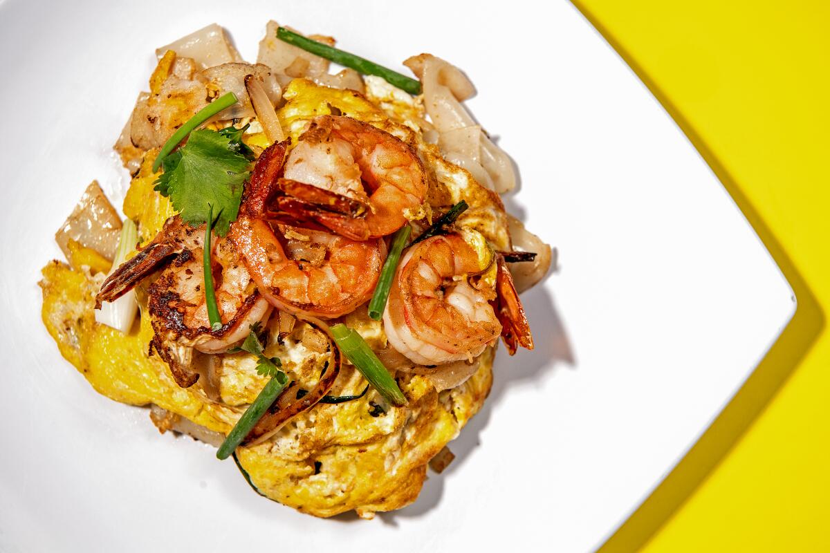 Shrimp and noodles on a white plate against a yellow background.