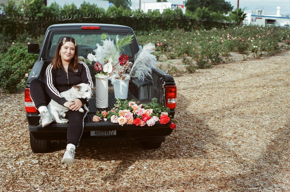 Floral designer Alex Floro sits in the bed of a truck parked in a field. She is surrounded by flowers. 