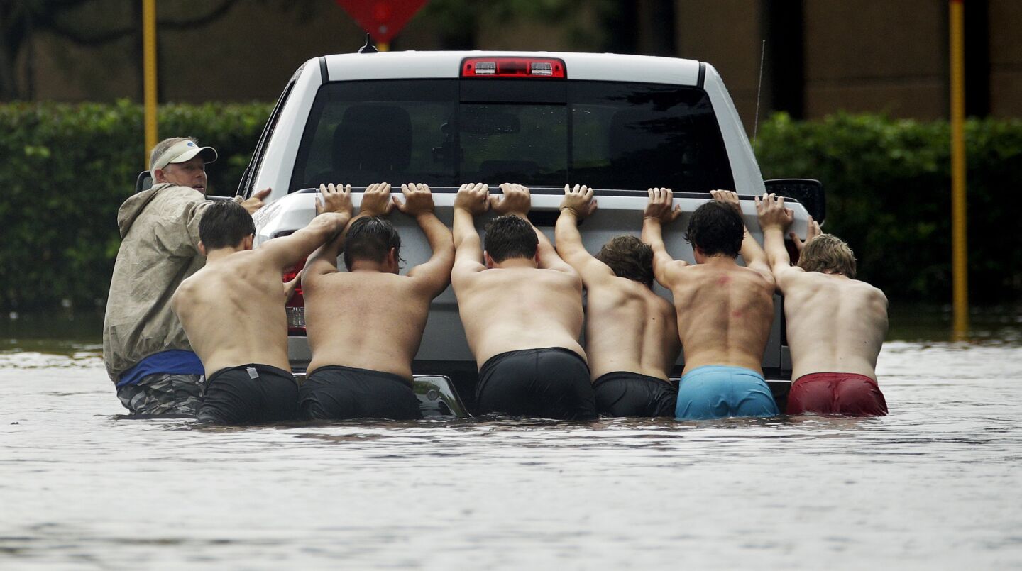 People push a stalled pickup to through a flooded street in Houston on Sunday, as Tropical Storm Harvey dumped heavy rains.
