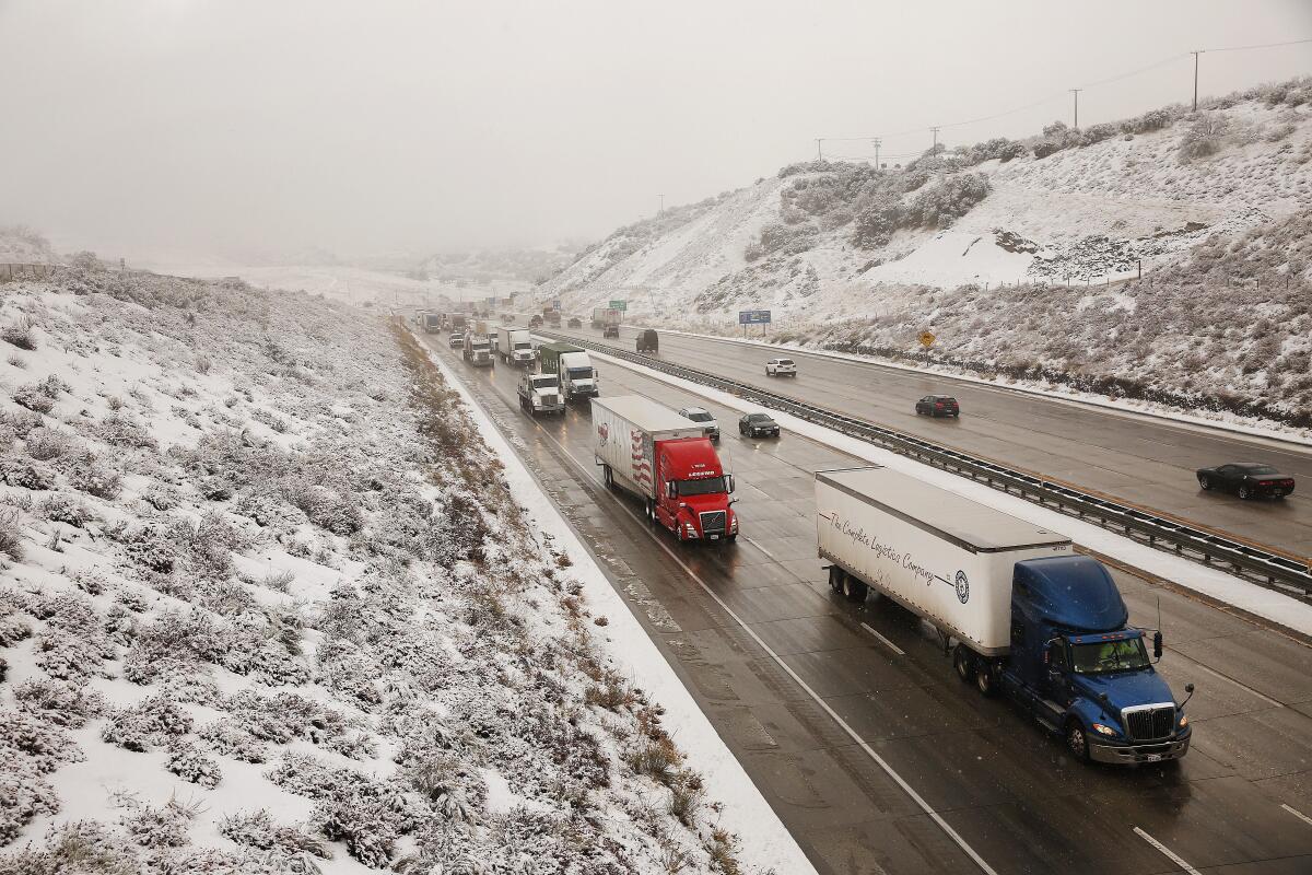 Cars and trucks drive on a freeway flanked by snowy hills. 