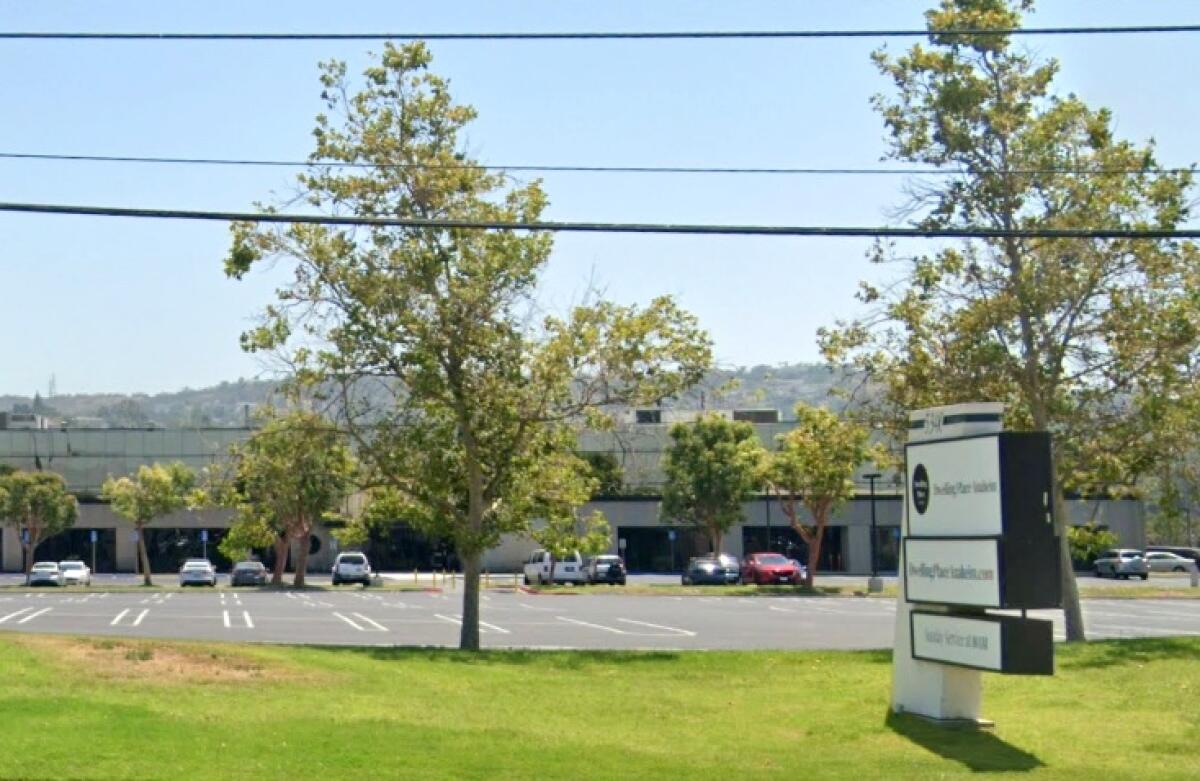 A building is seen behind a parking lot and a lawn area