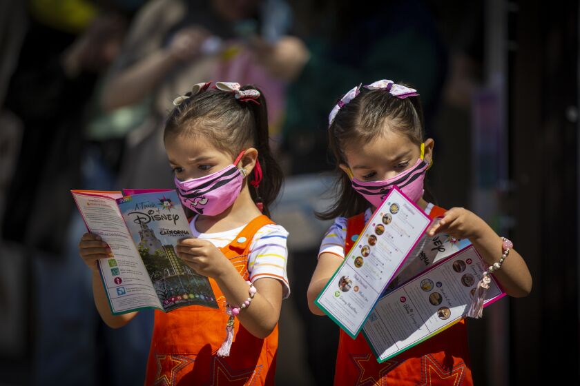 ANAHEIM, CA - March 18: Three-year-old twins Abigail Flores, left, and Aubrey Flores look at maps upon arrival of the debut of Disney California Adventure's "A Touch of Disney" food event at Disney California Adventure Park Thursday, March 18, 2021 in Anaheim, CA. This spans the entire DCA park and allows guests to eat, interact with characters and explore the grounds. A Touch of Disney, the new limited-time ticketed experience at Disney California Adventure Park which has sold out, takes place March 18 through April 19, 2021. (Allen J. Schaben / Los Angeles Times)