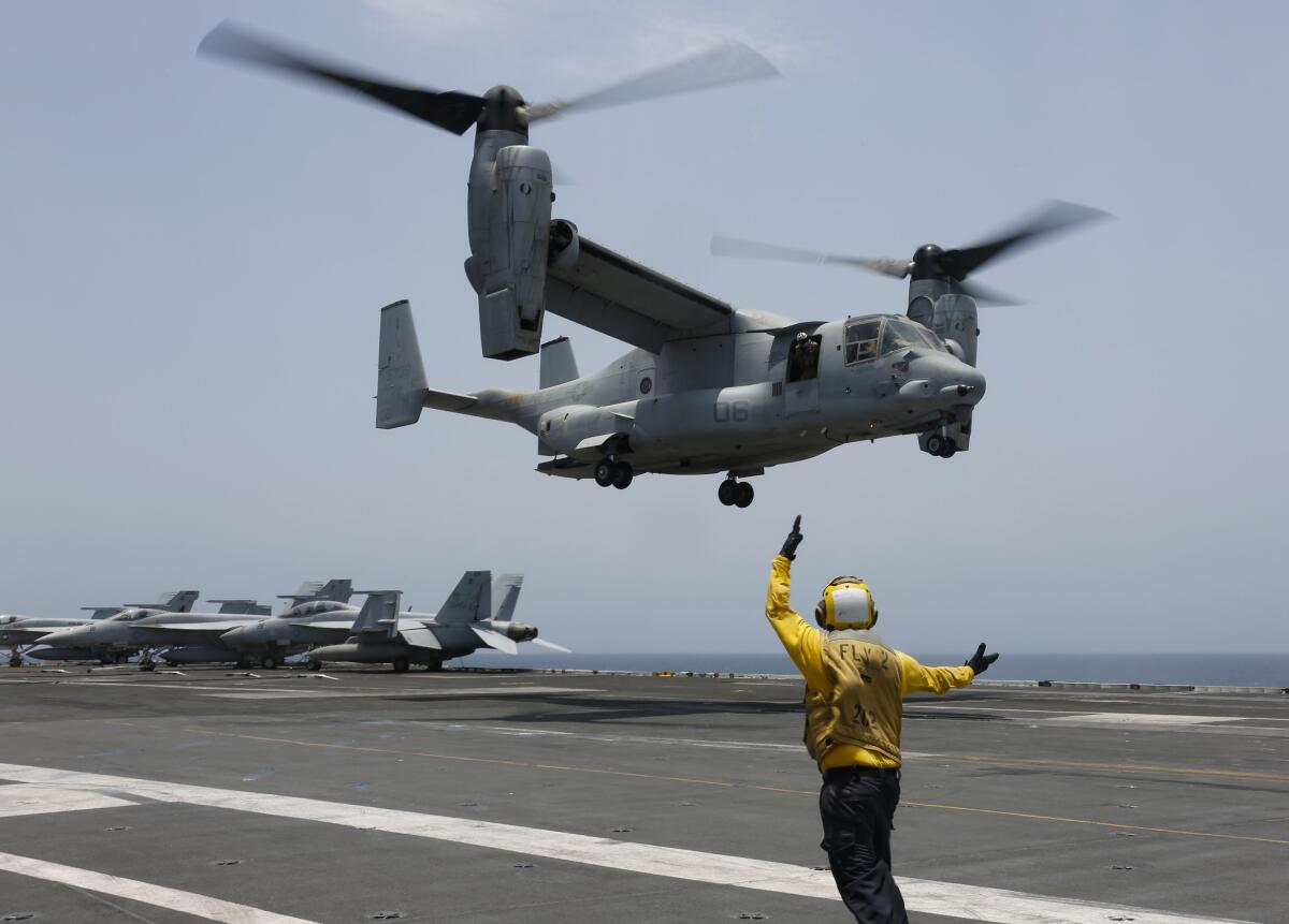 An MV-22 Osprey is signaled by a person to land on the flight deck of the USS Abraham Lincoln
