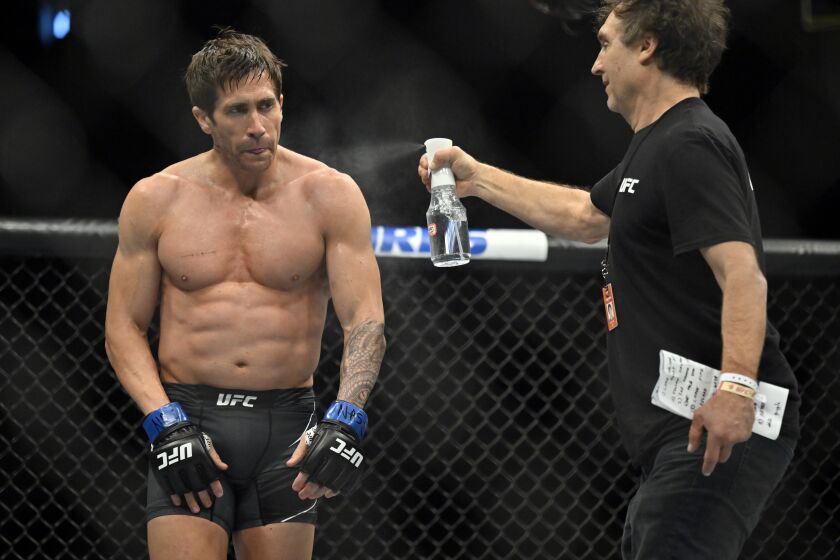 times batman review A man in a black outfit spraying a shirtless man in a boxing ring
