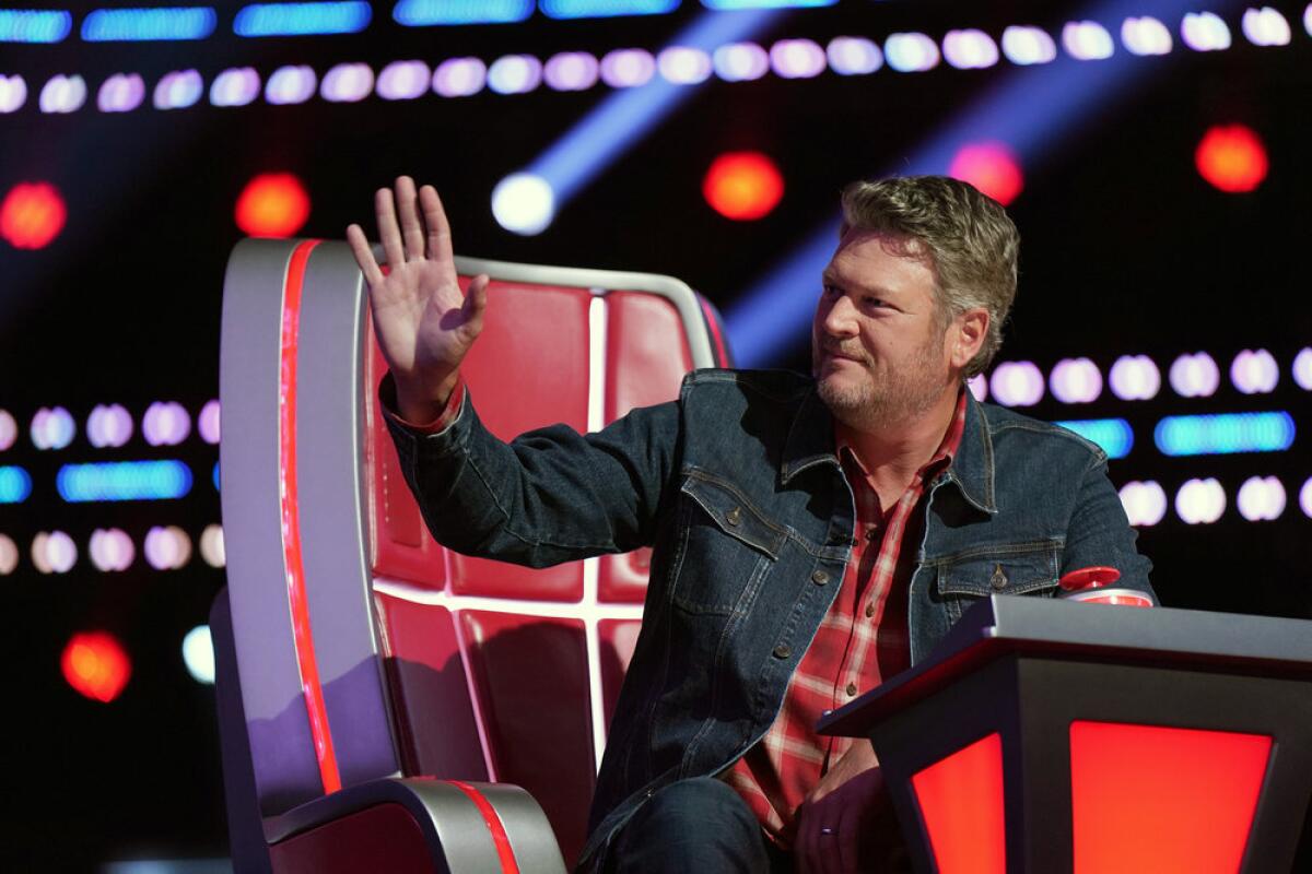 Blake Shelton in a red flannel shirt and denim jacket, sitting in a large chair