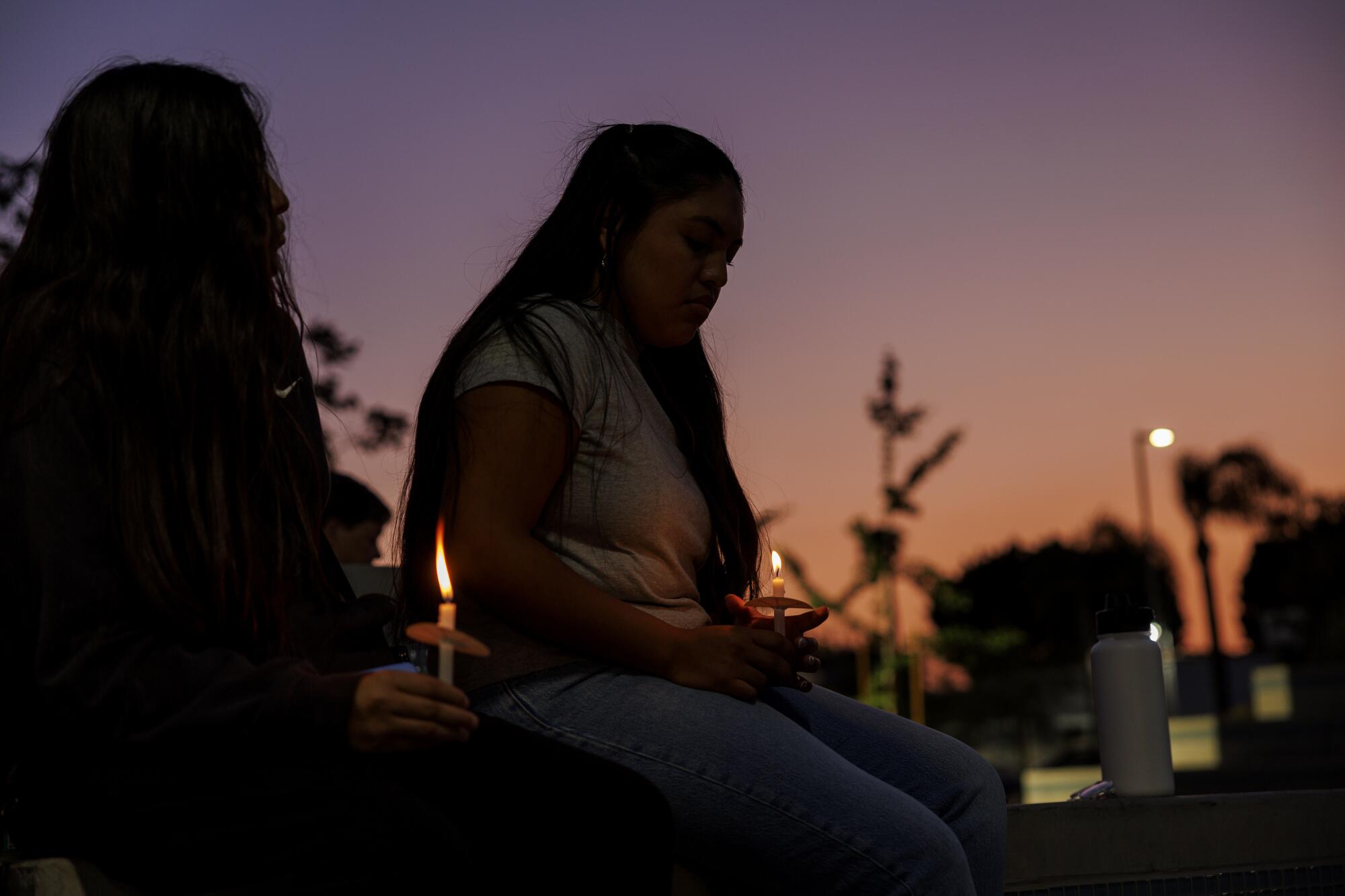 The list of two young women keeps small candles against sunrise.