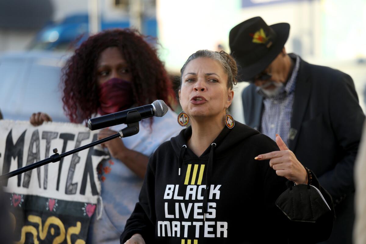 A woman speaking into a microphone wears a shirt that says "Black Lives Matter."
