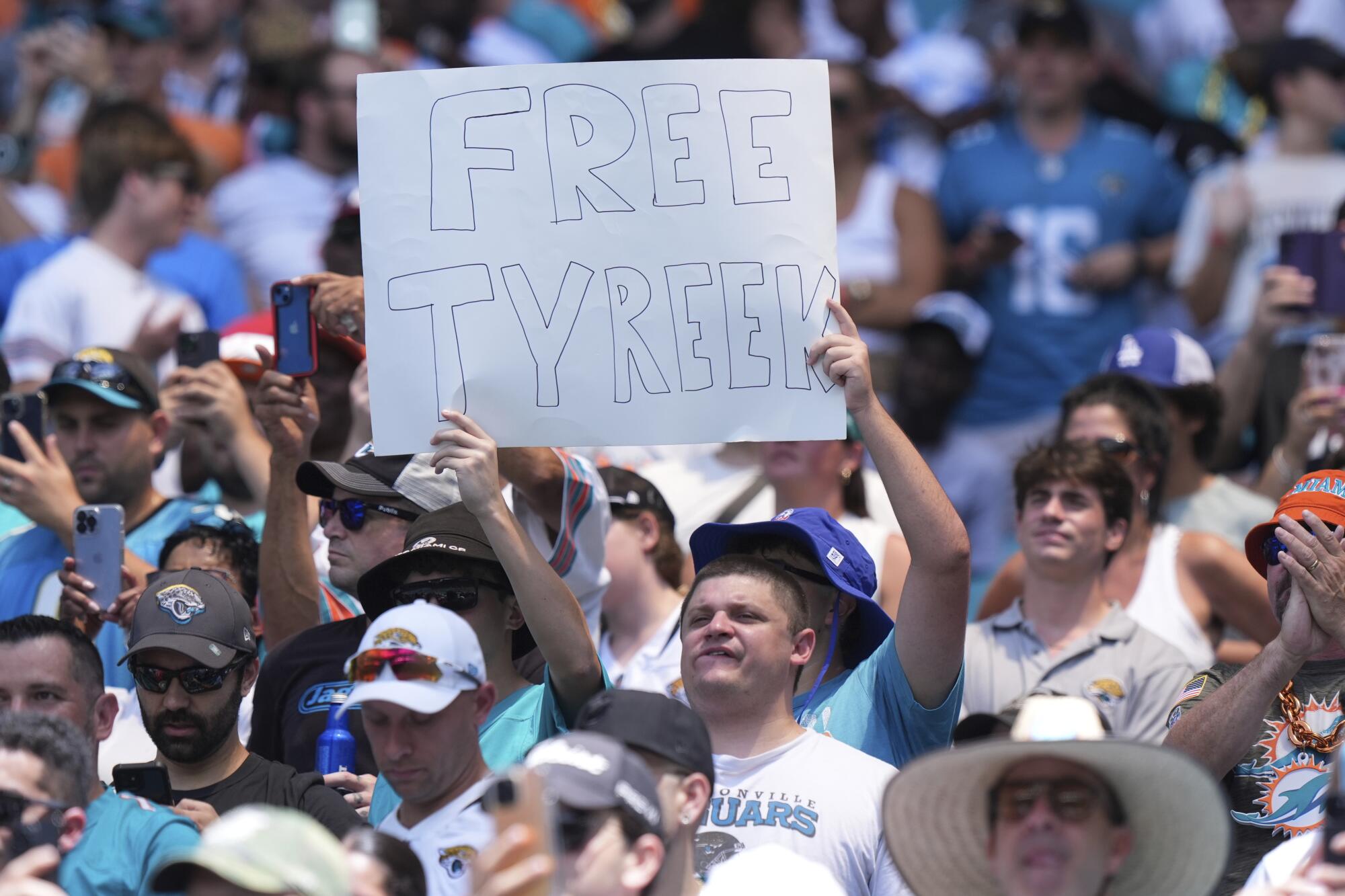 Amid a crowd in a stadium, a person raises a handmade poster that reads "Free Tyreek."