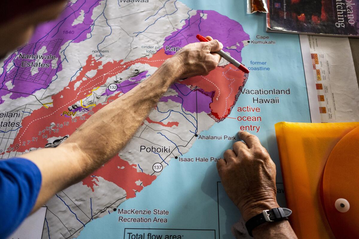 John Stallman points with a pen to areas where lava has expanded the coastline while talking with Jerry Dunn at "The Hub," a distribution center in Pahoa run by the community group Pu'uhonua o Puna to help evacuees.