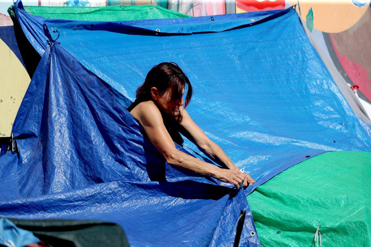 A woman tying a tarp at a homeless encampment at El Centro.