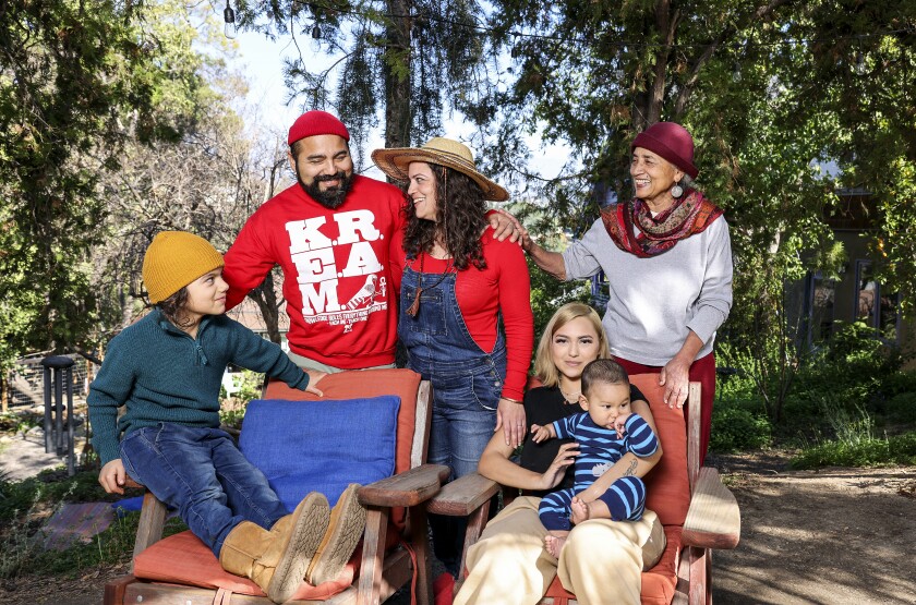 A portrait of a family — a baby sitting on a woman's lap, another young child and four adults — with a backdrop of trees.