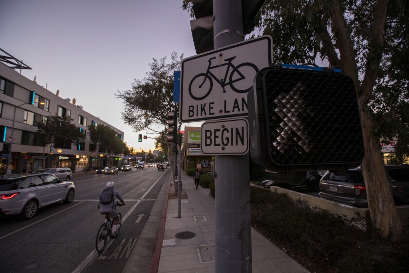 A bicyclist uses a bike lane next to a traffic signal and bike lane sign