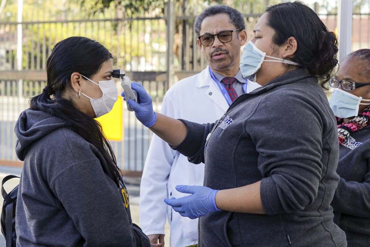 Dr. Oliver Brooks looks on as healthcare worker Lucy Arias checks a patient for fever at a coronavirus screening center at Watts Health Center.
