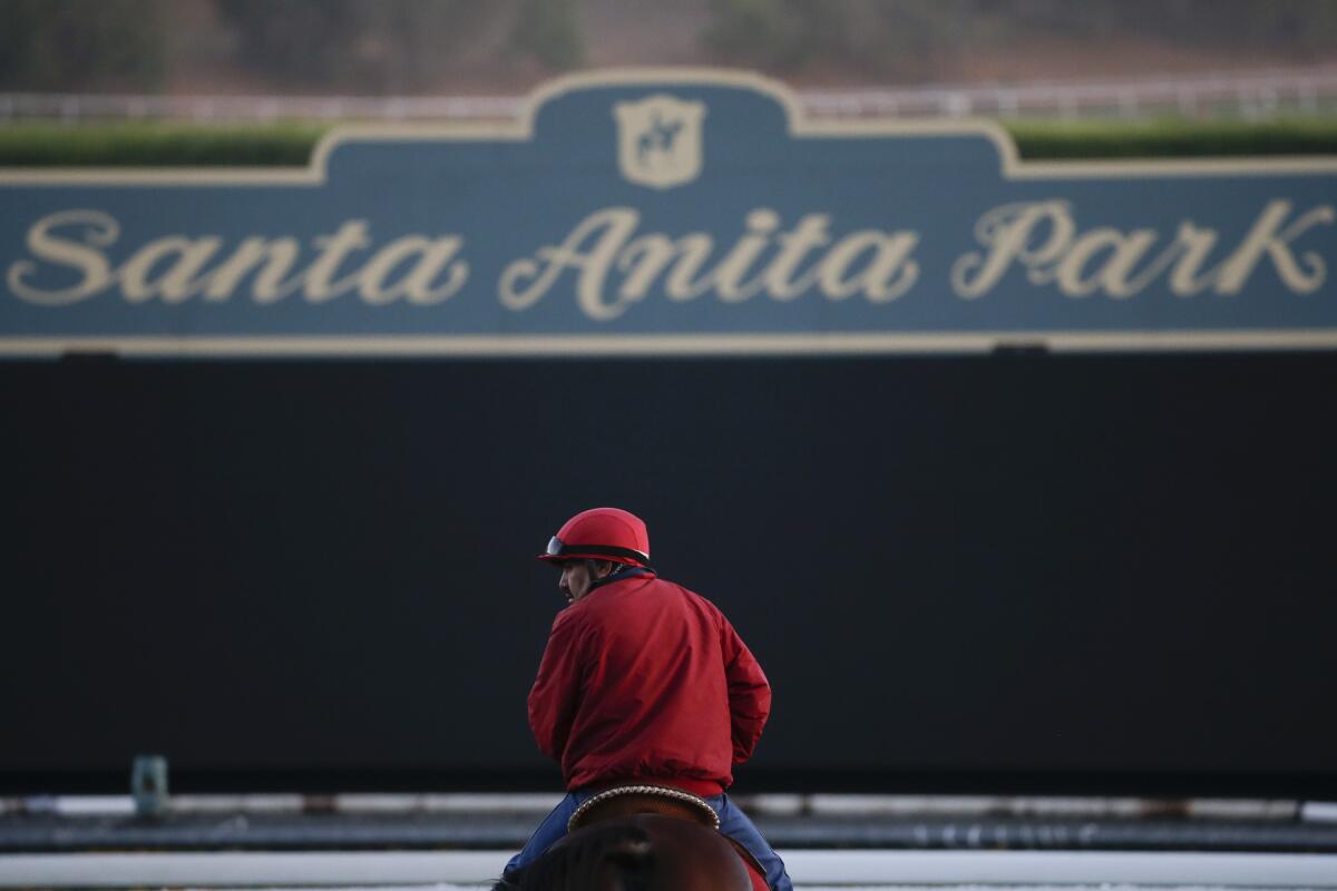 A rider atop a horse in front of a sign for Santa Anita Park.