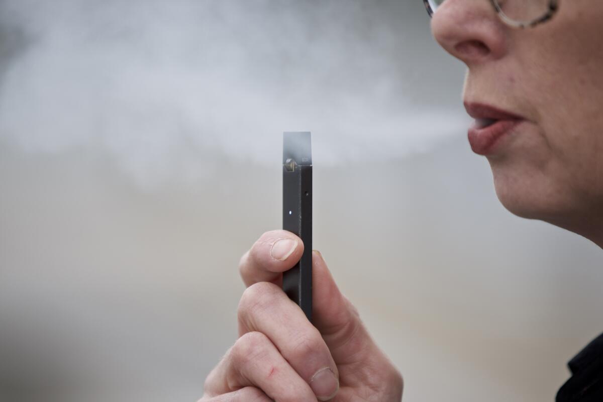 A woman exhales a puff of vapor from a Juul pen 