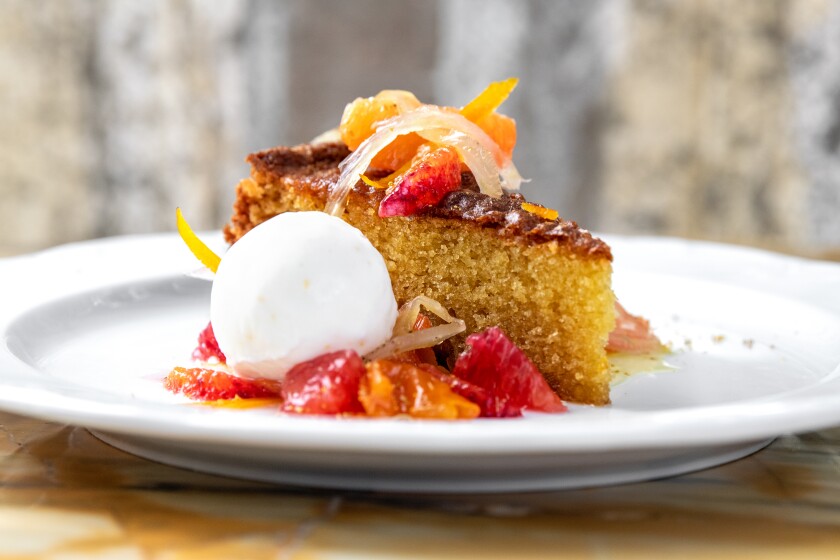 A piece of un-iced cake on a plate with glistening pieces of fruit on it.