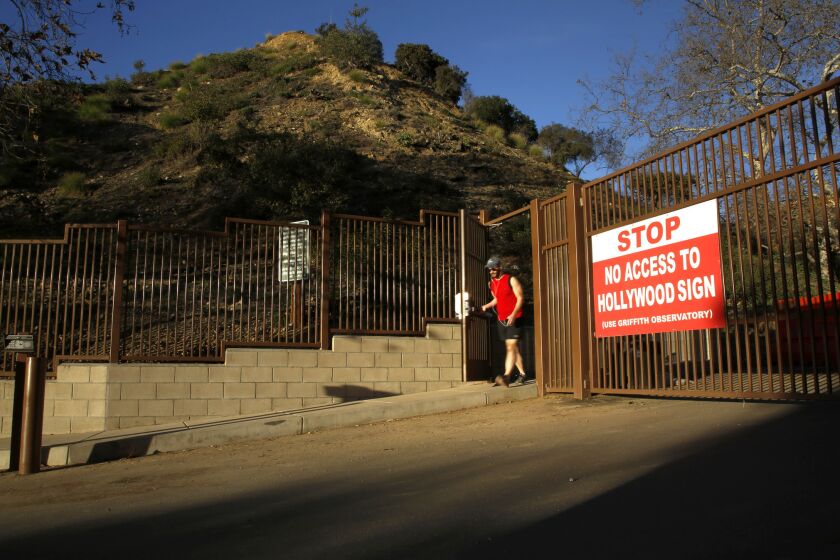 A runner walks out of a gate that leads to a hiking path that offers views of the Hollywood sign. The path reopened Monday after an electric gate was installed that will limit car traffic going up the trail, but will give hikers access during the park's hours.