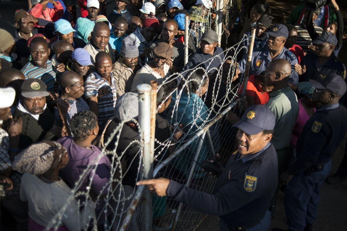 South African police guard a gate as striking platinum miners and their relatives line up to get food parcels from the South African food bank on June 13.