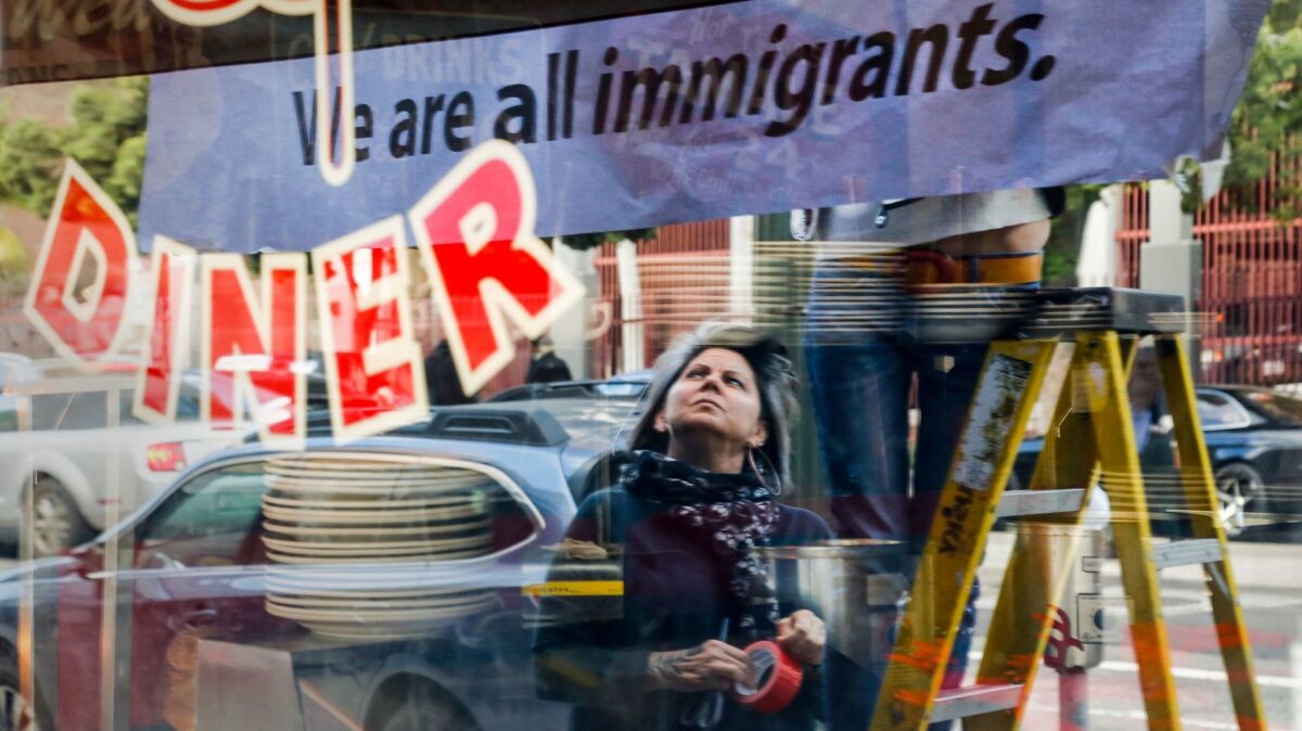 After closing their restaurant for the day, Monica May watches while her partner Kristen Trattner hung a sign above their Nickel Diner in Downtown Los Angeles in solidarity with a national "Day Without Immigrants."