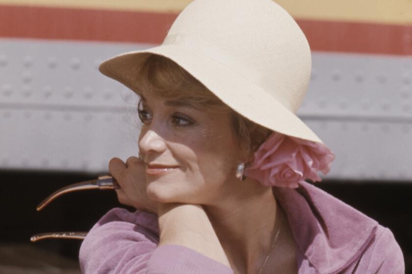 Lynne Marta, in a hat, has a relaxed smile as she rests her head on her arm, her outstretched foot rests on a metal rail