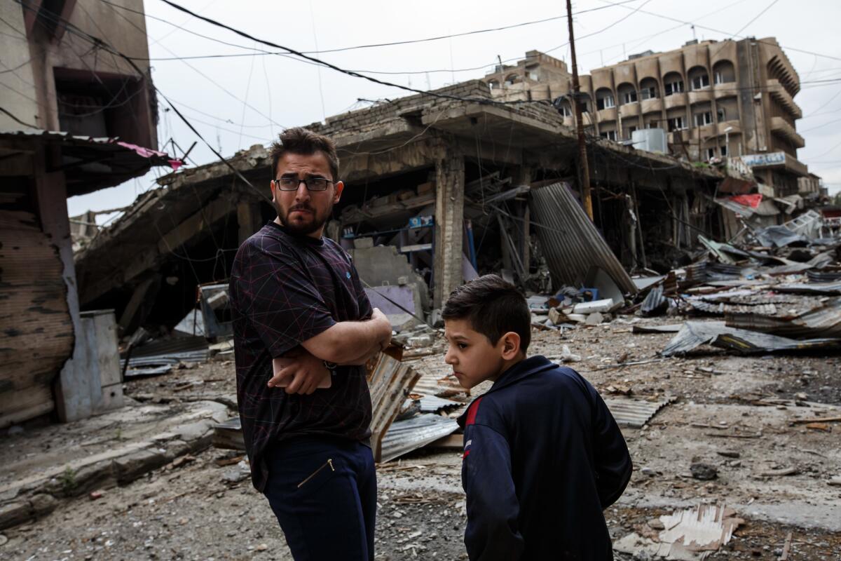 Ahmed Raed Kotiba, left, stands with his cousin outside a building destroyed by an airstrike in west Mosul's Dawasa neighborhood.