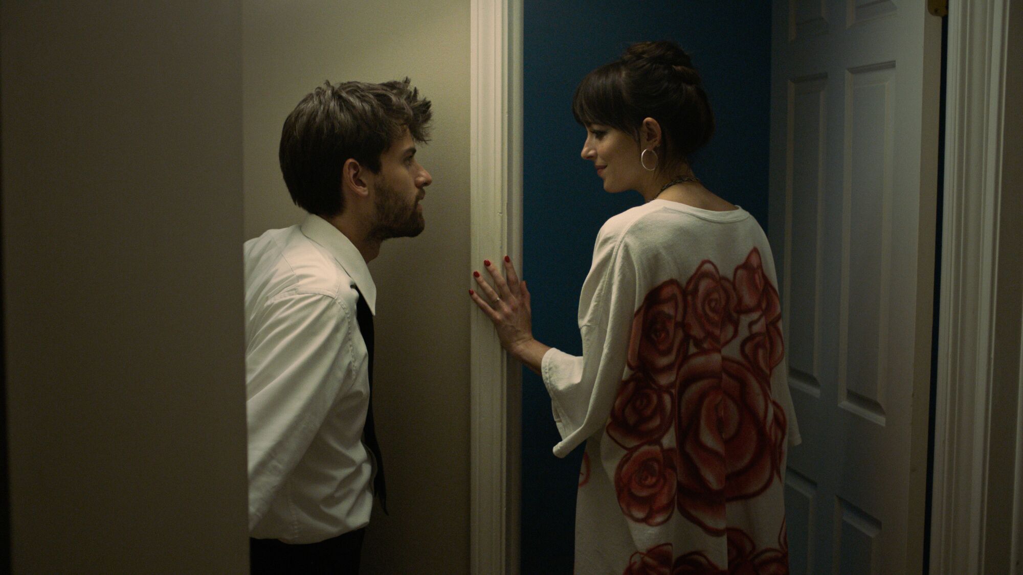 A man and a woman linger in a doorway, looking at one another.