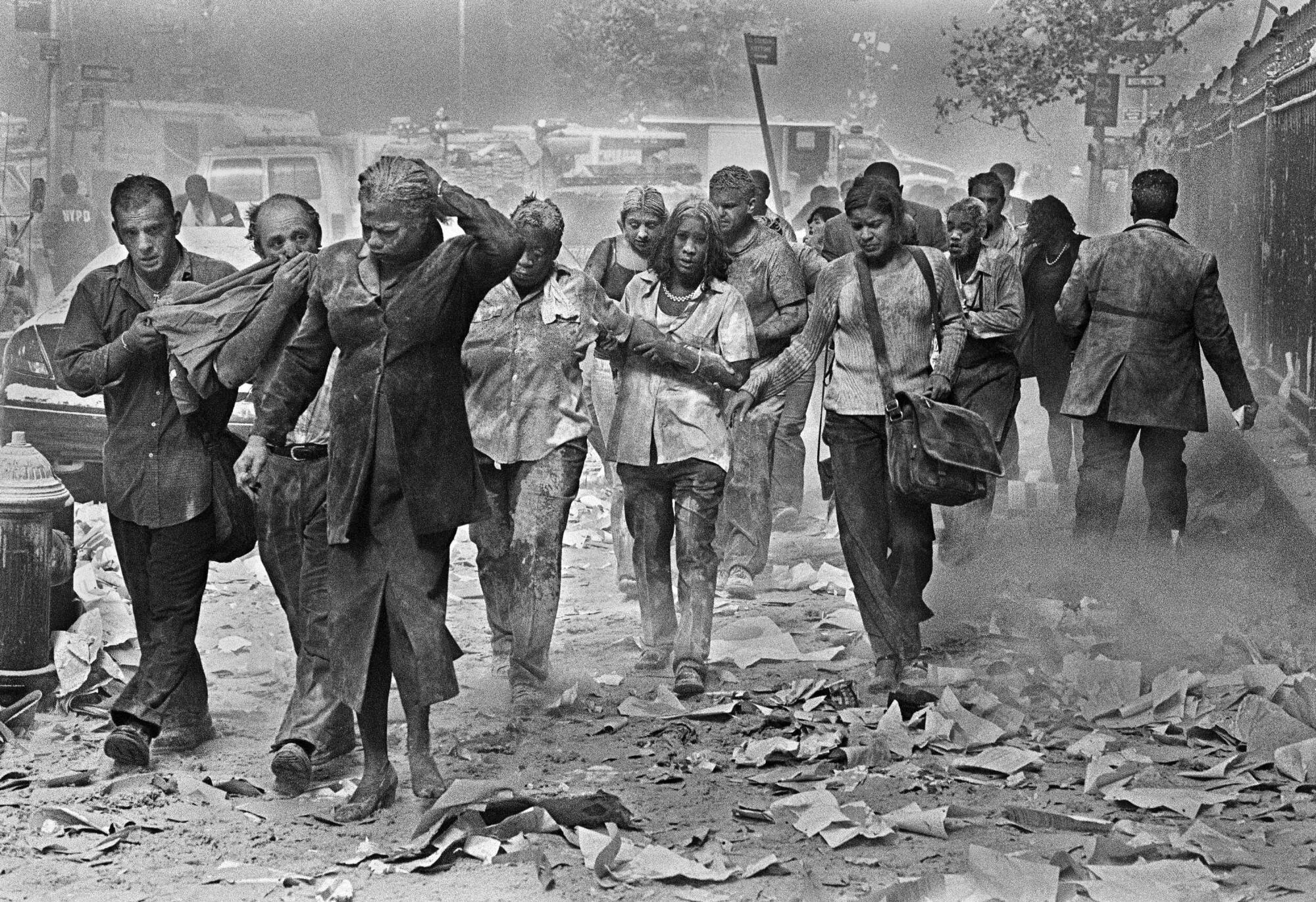 People covered in dust and surrounded by debris walk down a street