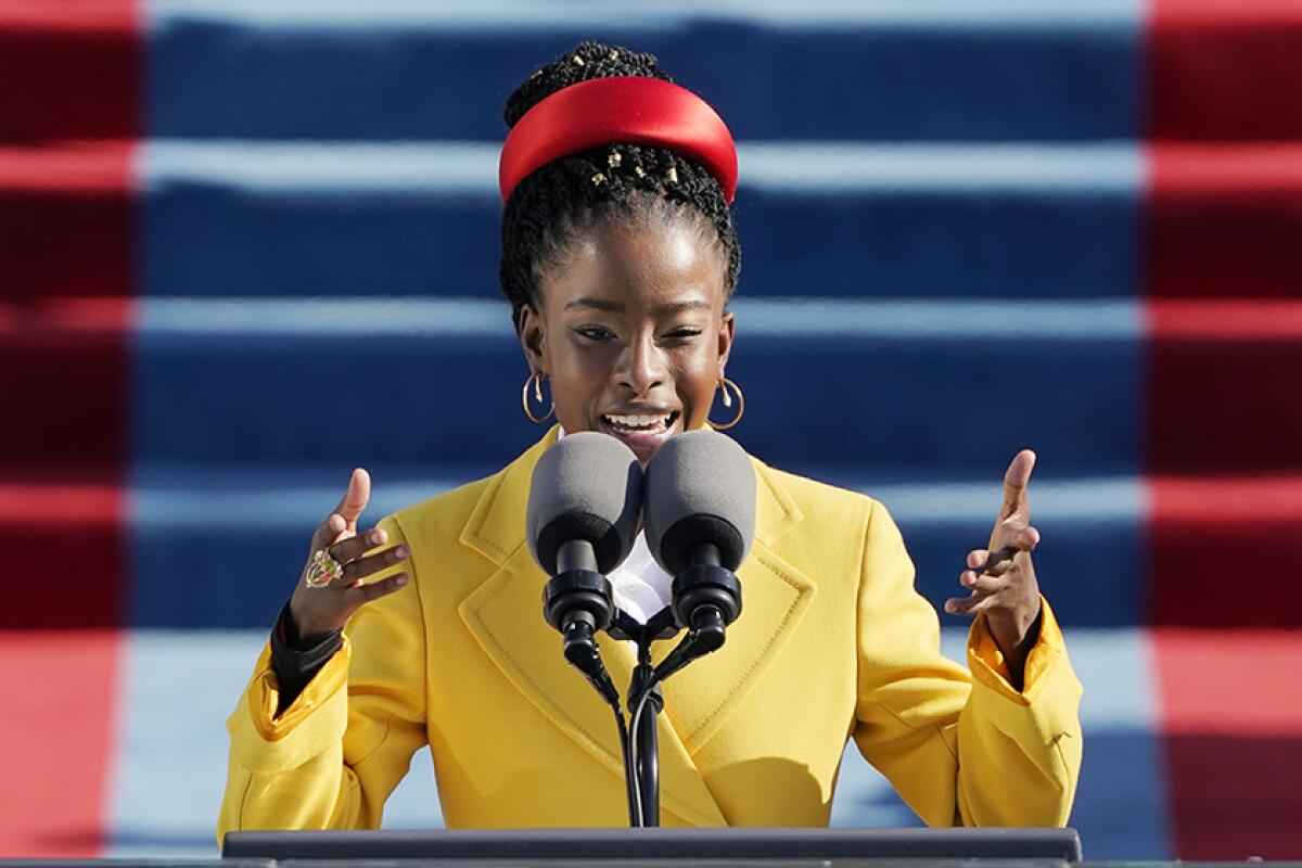 A young woman in a yellow coat gestures as she speaks at a podium.