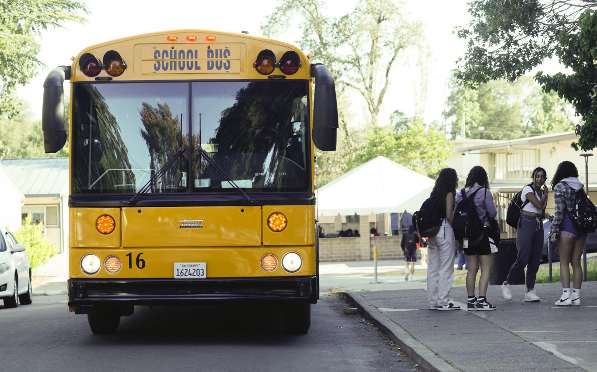 A yellow school bus alongside students in backpacks on a sidewalk.