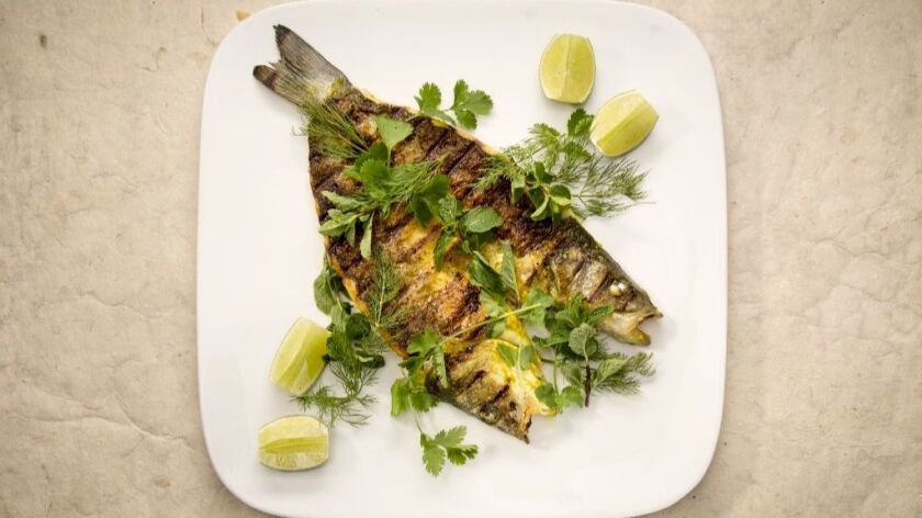 A whole grilled branzino on a white plate