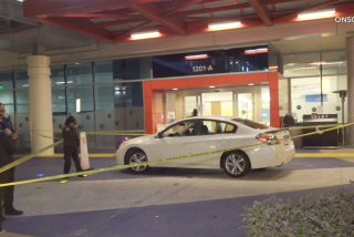 A car is surrounded by yellow police tape in front of a hospital emergency room entrance.