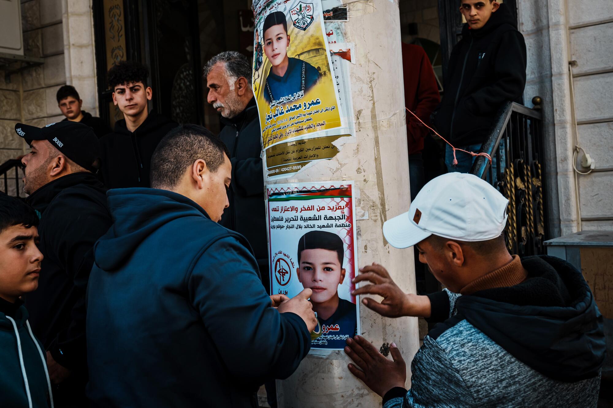 Des membres de la communauté aident à coller des affiches de martyrs à l'extérieur de la mosquée lors d'un cortège funéraire.
