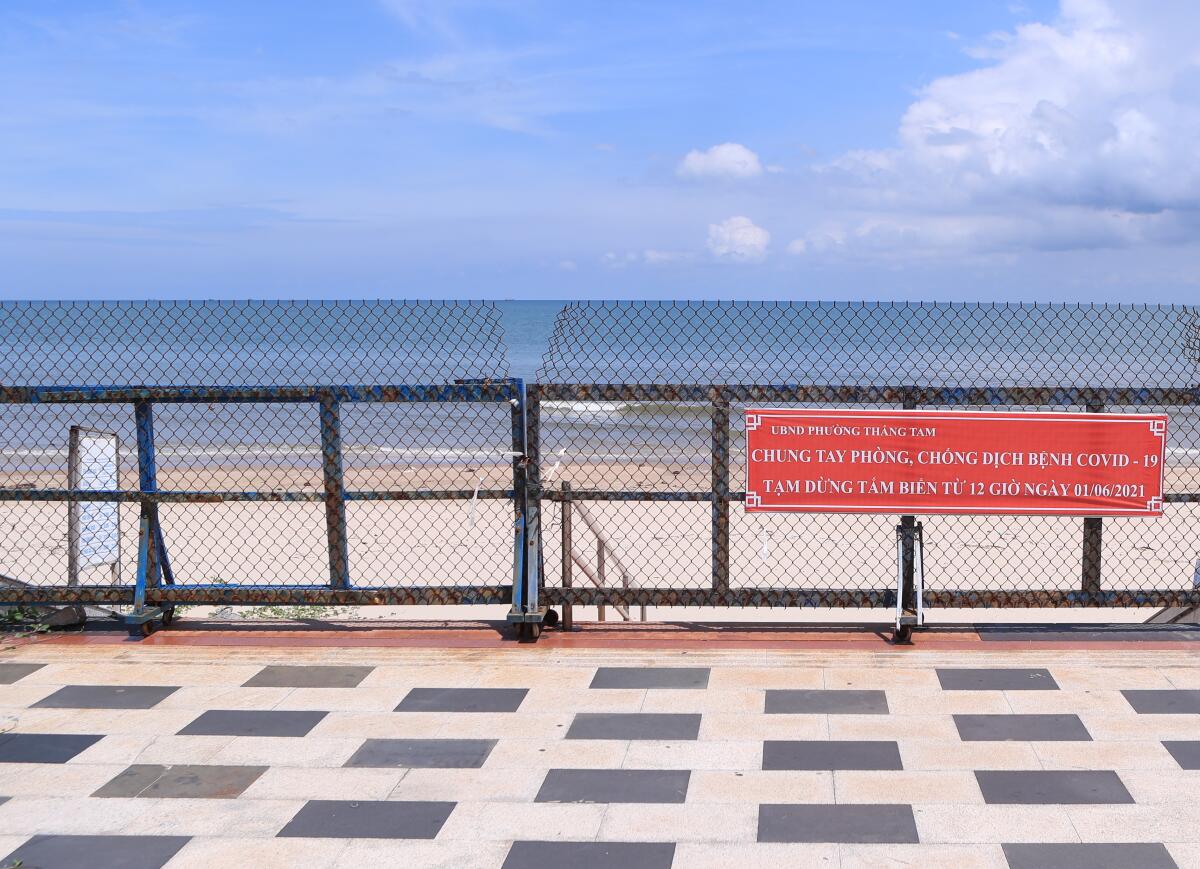 The entrance to a Vietnamese beach is barricaded with a sign that says, "Fight COVID-19 together, no beach activities."