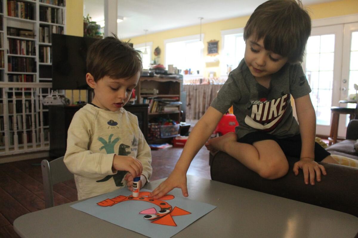 Two small boys use a glue stick to create an orange paper cat shaped like the letter C