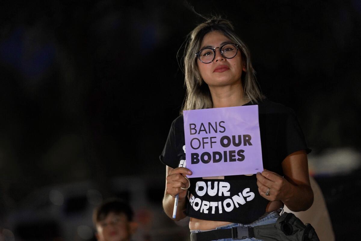 A woman holds a purple sign that says, "Bans Off Our Bodies"