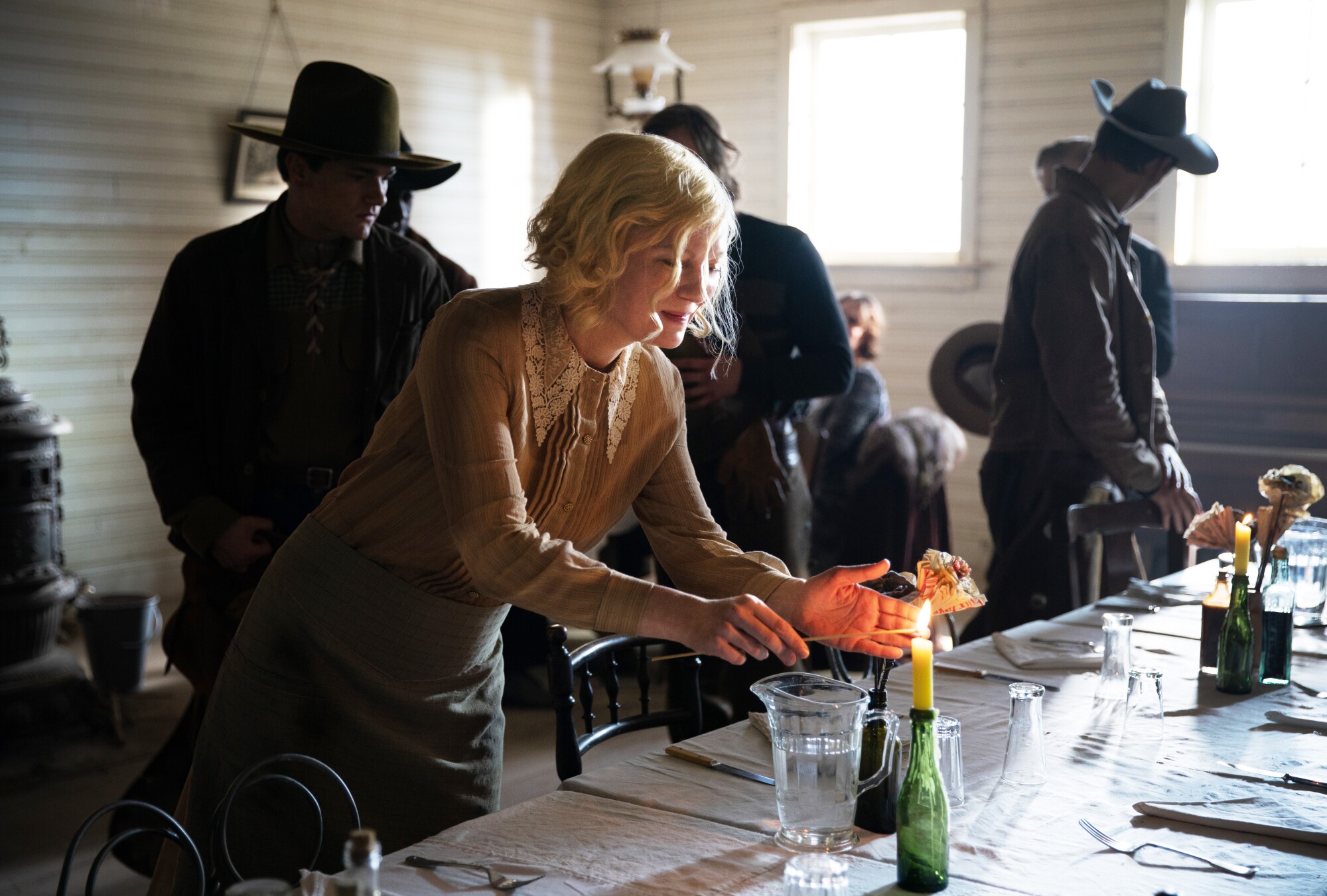 Eine Frau zündet eine Kerze auf einem Tisch an, während Cowboys hinter ihr stehen.