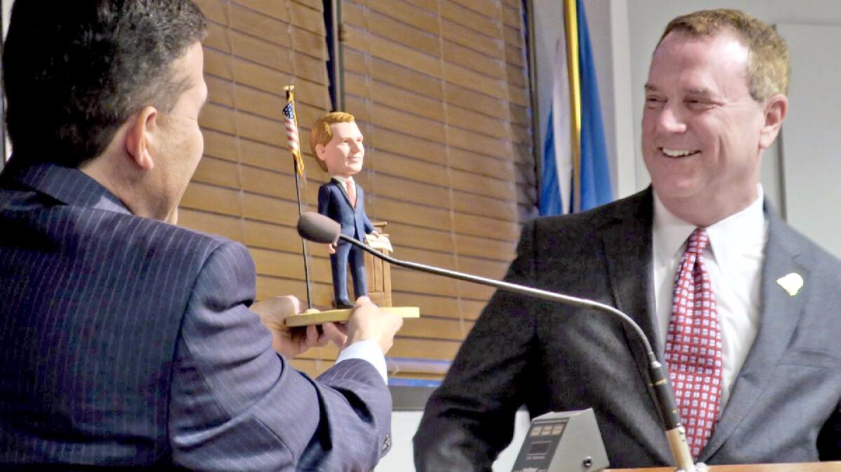 La Cañada Flintridge City Manager Mark Alexander, left, presents outgoing Mayor Jon Curtis with a bobblehead made in his likeness.