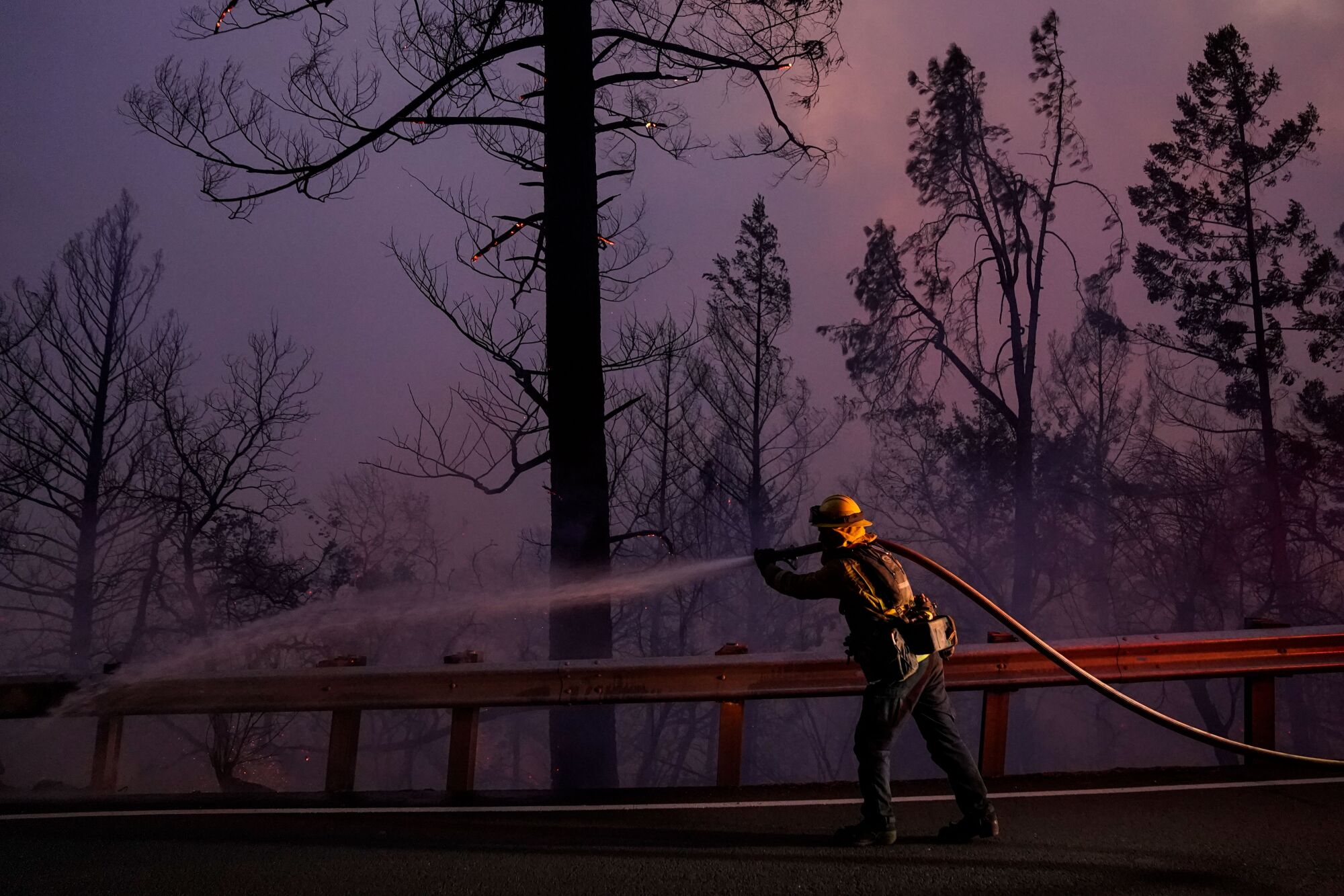 A firefighter sprays a hose amid smoky haze.