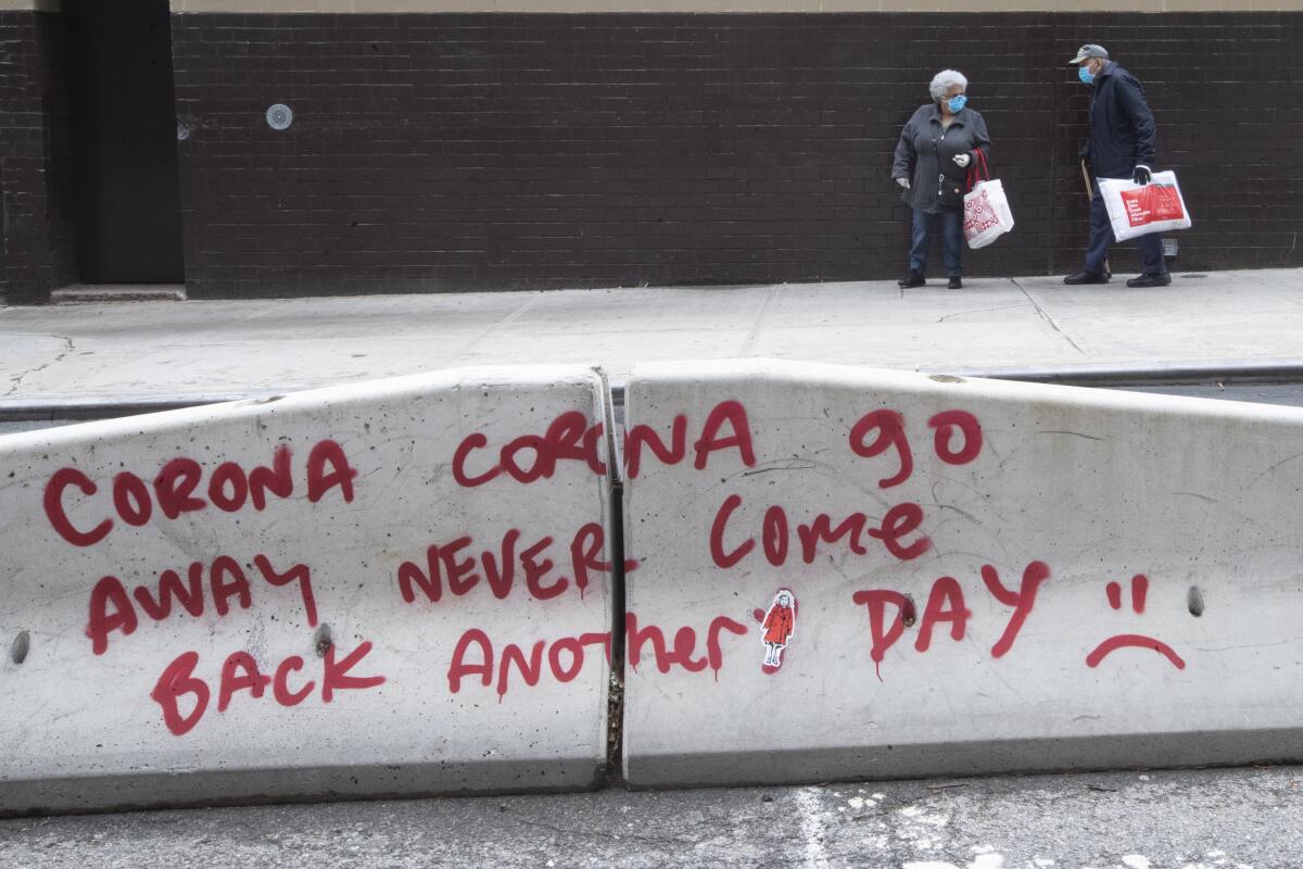 A couple in masks walk past coronavirus graffiti on a street divider on the Lower East Side of Manhattan on Monday. 