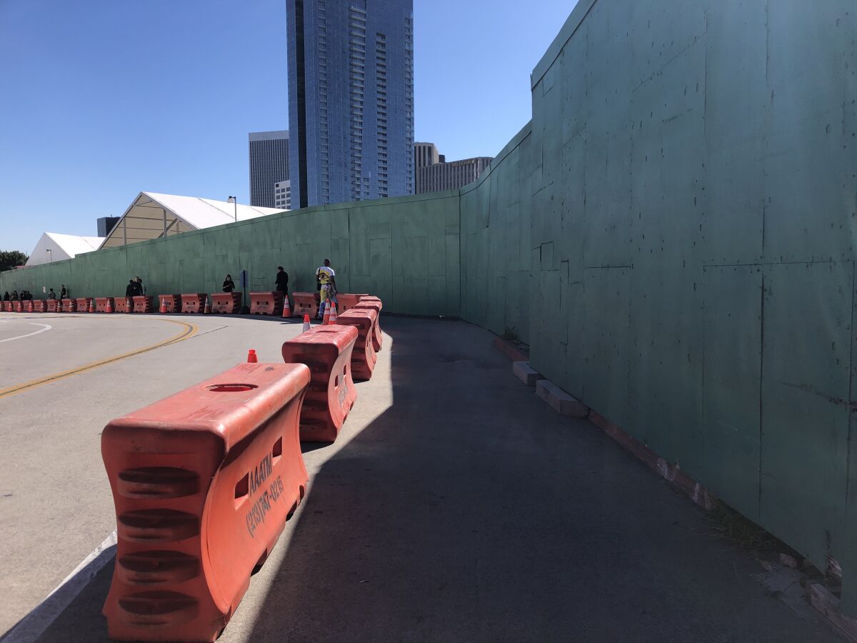 A street view shows a pedestrian path between plastic k-rails and a construction fence.