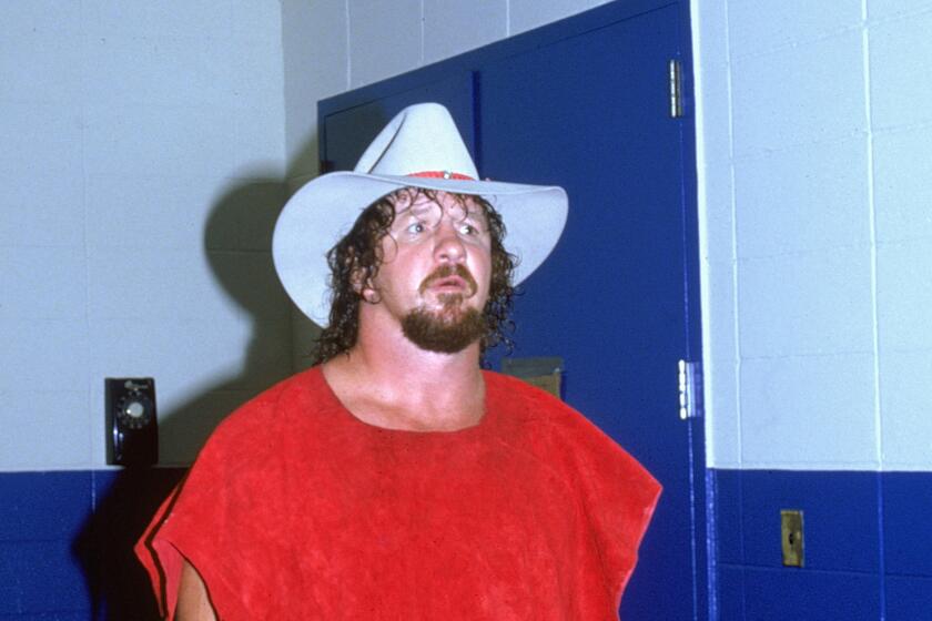 Wrestler Terry Funk wears a cowboy hat and looks down a hallway