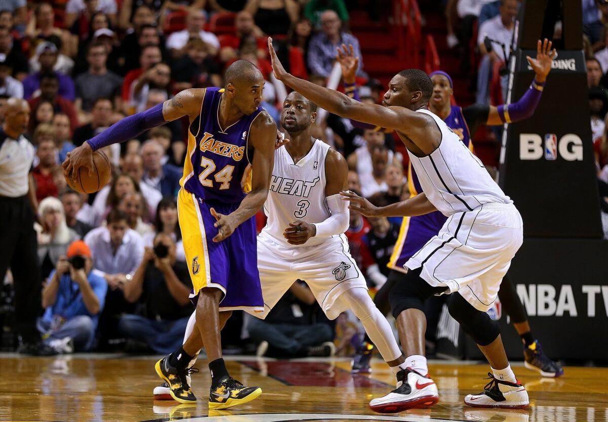 Lakers guard Kobe Bryant wraps a no-look pass behind his back to Dwight Howard (background) on Sunday, circumventing the defense of the Miami Heat's Dwyane Wade and Chris Bosh.