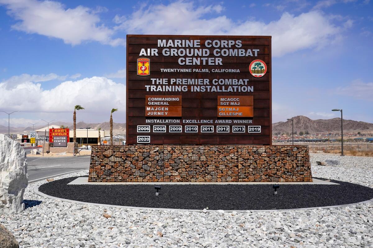A sign reads "Marine Corps Air Ground Combat Center." In the background are blue sky and clouds.