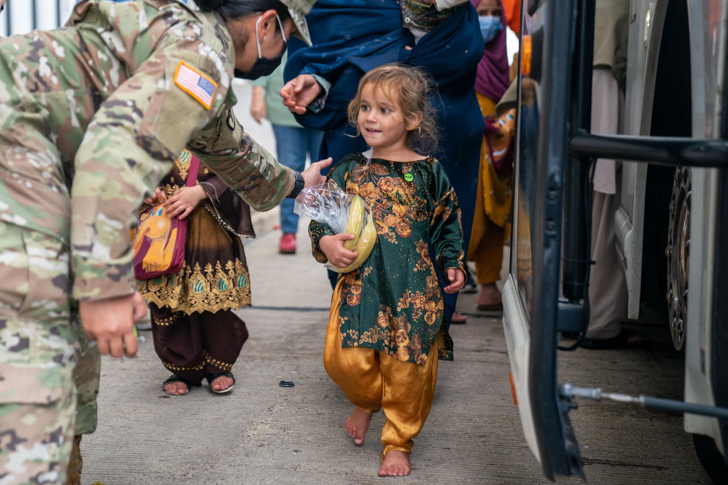 A U.S. service member greets a smiling child in a colorful outfit 